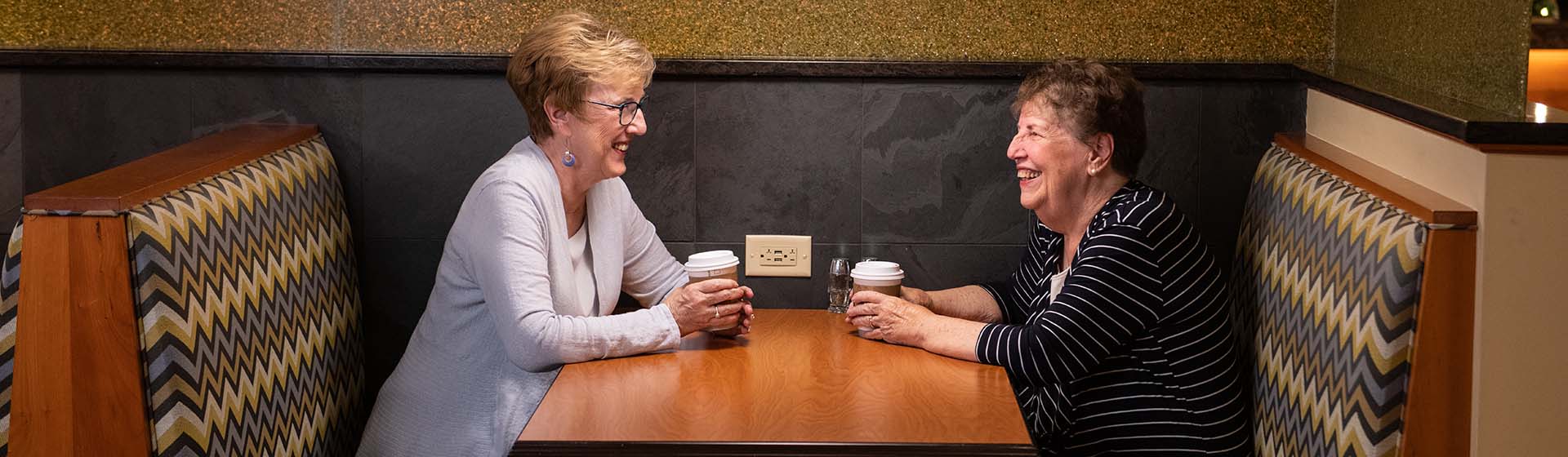 two women are sitting at a table in a booth drinking coffee