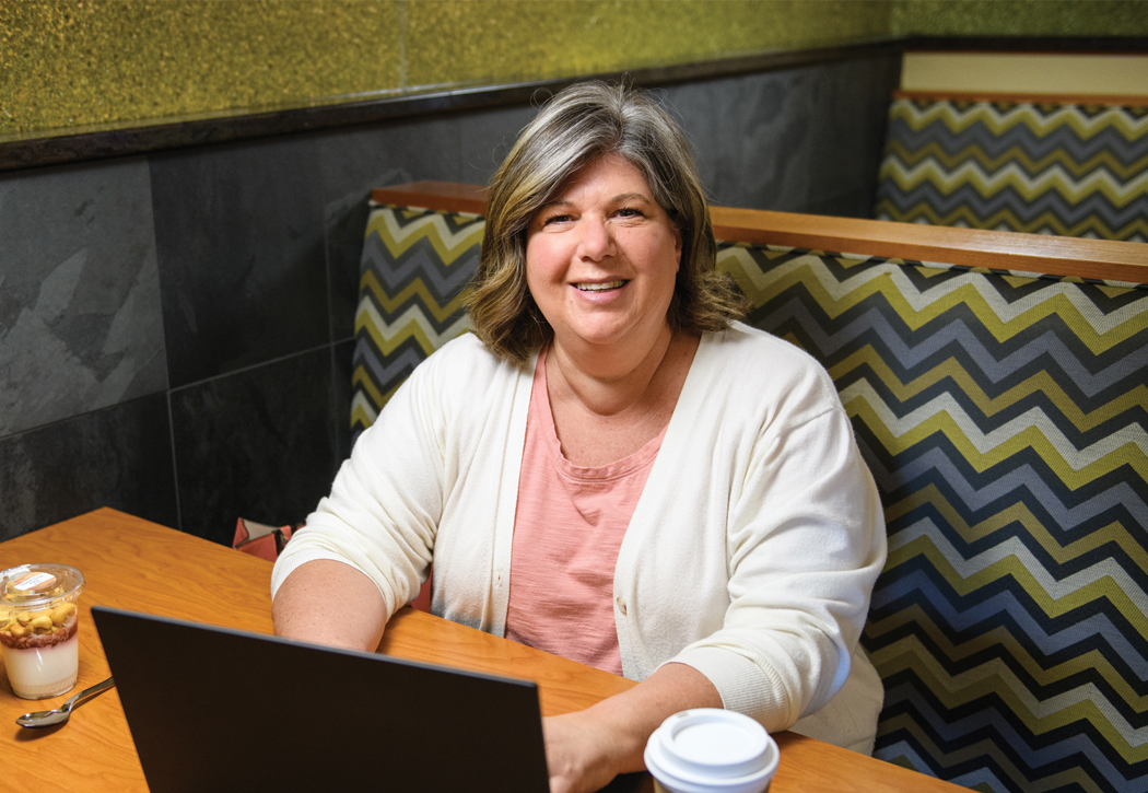 a woman sits at a table with a laptop and a cup of coffee